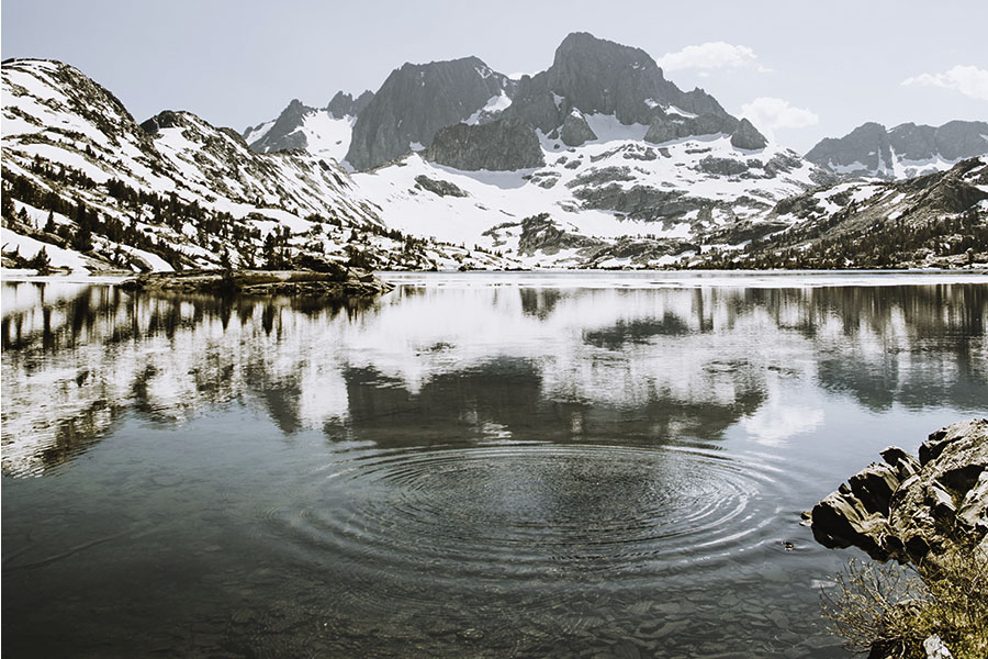 An alpine lake, with snow covered mountains, and ripples emanating in the lake.